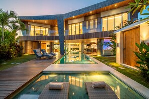 Ein modernes, zweistöckiges Haus mit Swimmingpool, Liegestühlen und einer Holzterrasse.