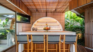A wooden bar area with a TV, a shelf with bottles, and a bowl of fruit. - Architect's 3BR Villa, Canggu (Canggu)