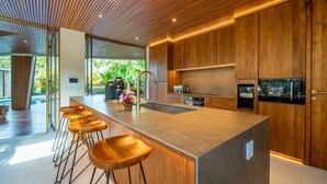 A modern kitchen with a central island, wooden bar stools, and built-in appliances. - Architect's 3BR Villa, Canggu (Canggu)