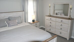 A bedroom with a bed, a dresser, a mirror, and a nightstand with a lamp.