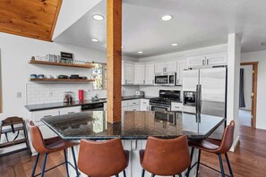A modern kitchen with white cabinets, a central island with bar stools, and built-in appliances. - Wolf Den Cabin • Spa • Walk to Lake (Big Bear Lake)