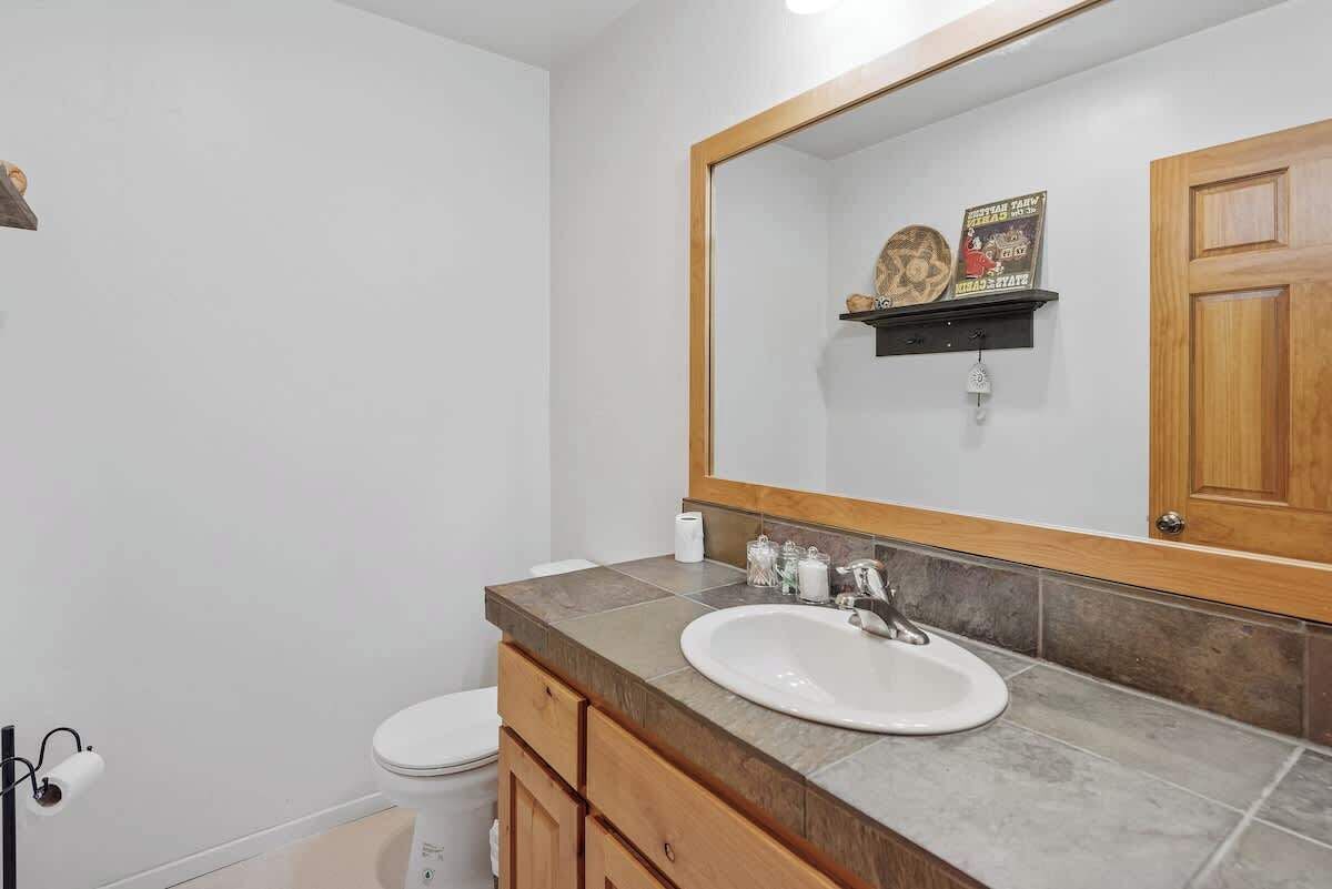 Un baño con inodoro blanco, lavabo con espejo grande y mueble de madera.