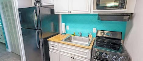 A compact kitchen with white cabinets, a black refrigerator, a microwave, a stove, and a sink.