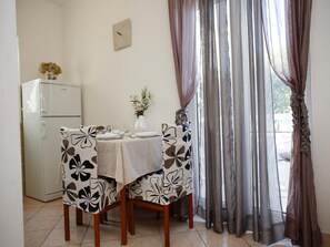 A dining area with a table set for two, a refrigerator, and a vase with flowers.