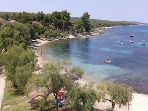 A coastal area with clear waters, boats, and a beach with trees and buildings in the background.