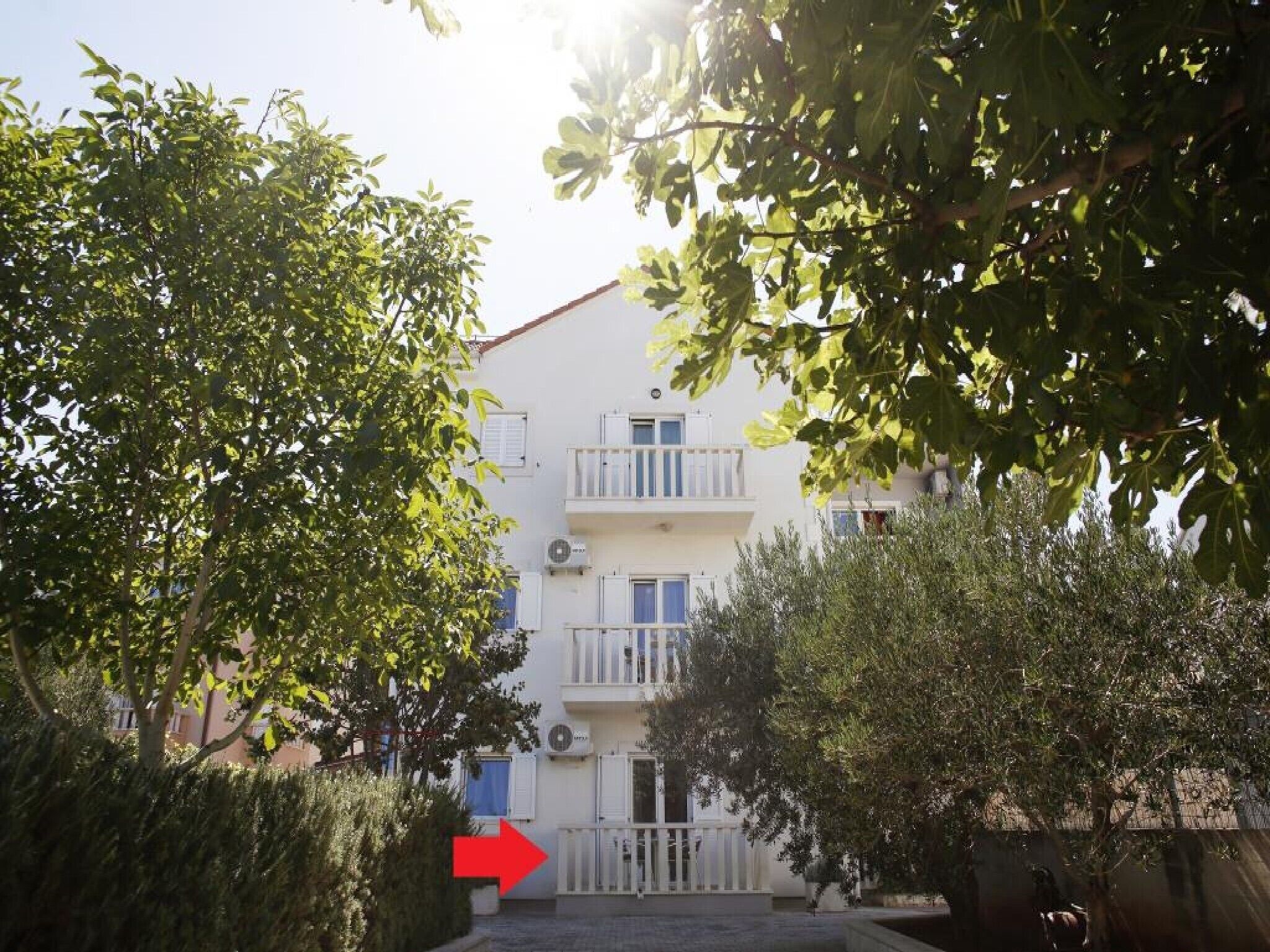 A two-story building with balconies, surrounded by greenery.
