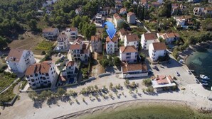 Vista aerea di una zona residenziale costiera con numerose case a due piani, una spiaggia sabbiosa e un cielo azzurro e sereno.