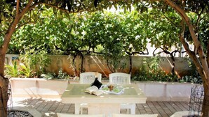 Patio esterno con tavolo e sedie, circondato da piante e alberi.