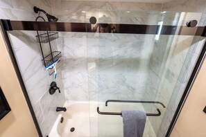 Ein modernes Badezimmer mit einer gläsernen Duschkabine, Marmorfliesen, einem Handtuchhalter und einer kleinen Ablage mit Toilettenartikeln.