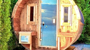 A wooden cabin with a circular design, a door, and a small window. - Lakefront vacation home with private beach & sauna – Villa Noho (Nonnenhorn)