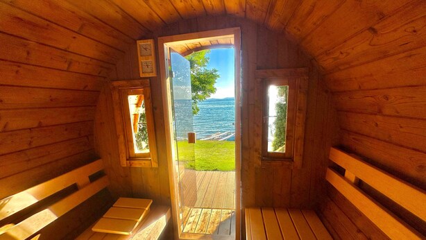 A wooden cabin with a bench and a door leading to a deck with a view of the water. - Lakefront vacation home with private beach & sauna – Villa Noho (Nonnenhorn)
