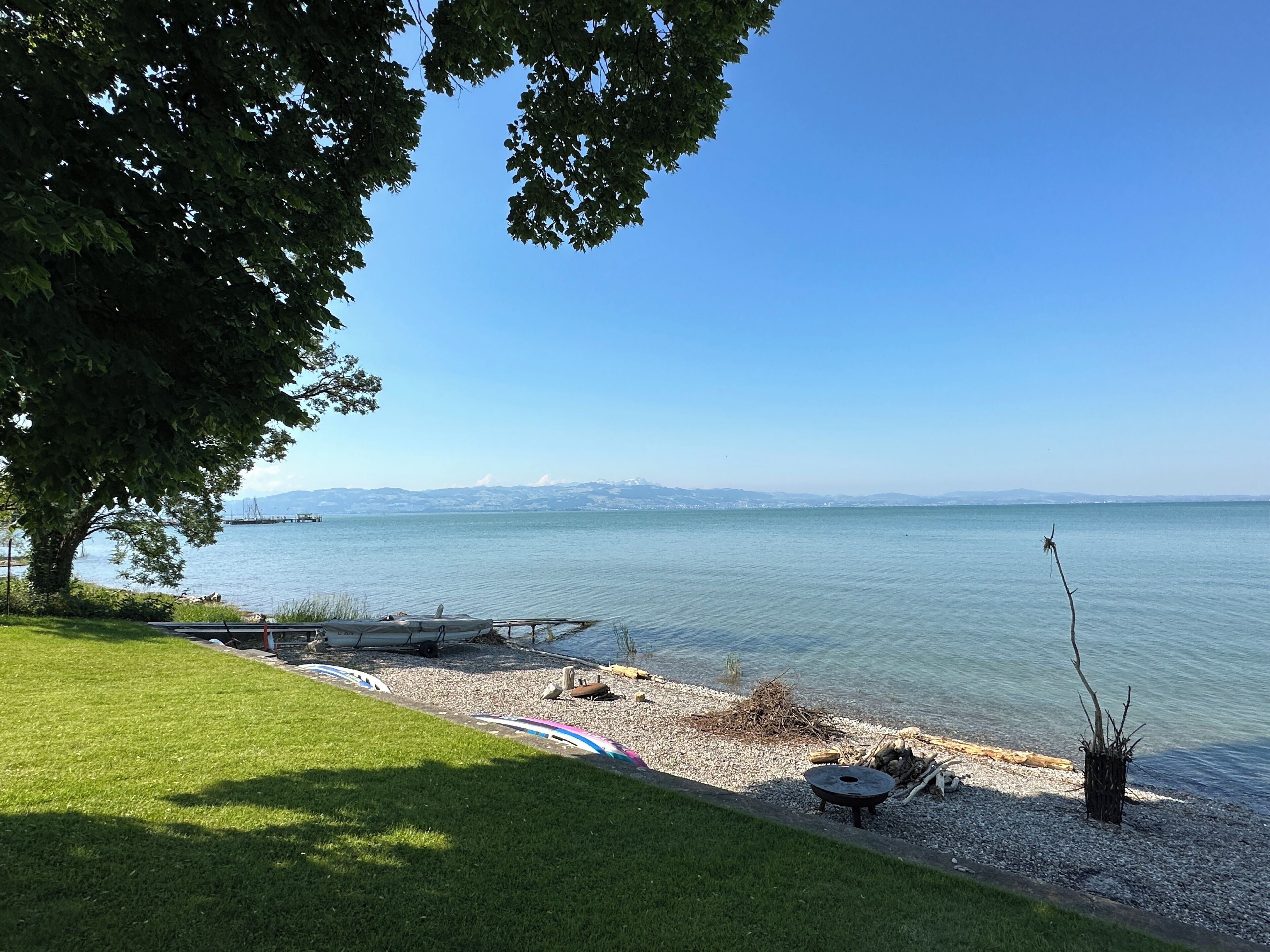 Blick auf einen See mit einer Rasenfläche, einem Steg und blauem Himmel.
