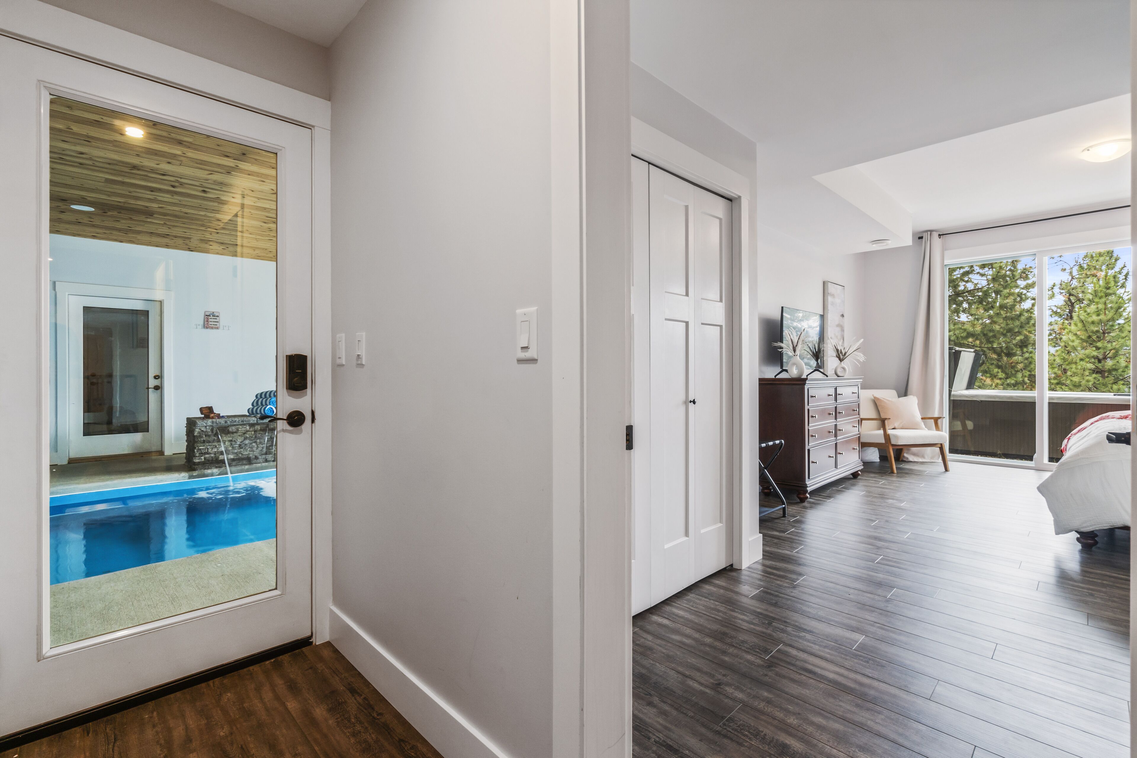 Un intérieur moderne avec un plancher en bois, une porte blanche donnant sur un balcon et une vue sur une piscine.