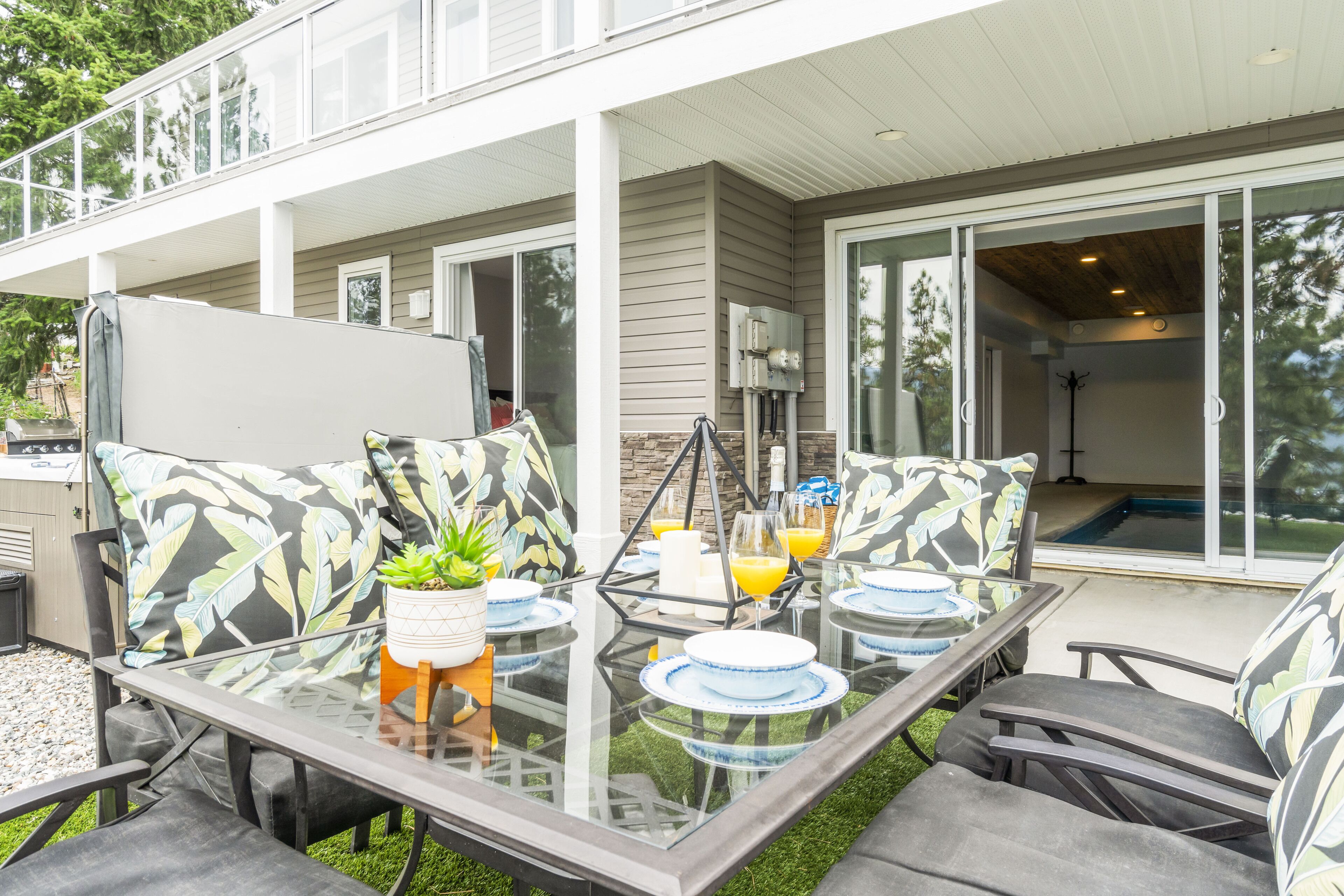 An outdoor patio area with a glass table set for dining, surrounded by cushioned chairs.