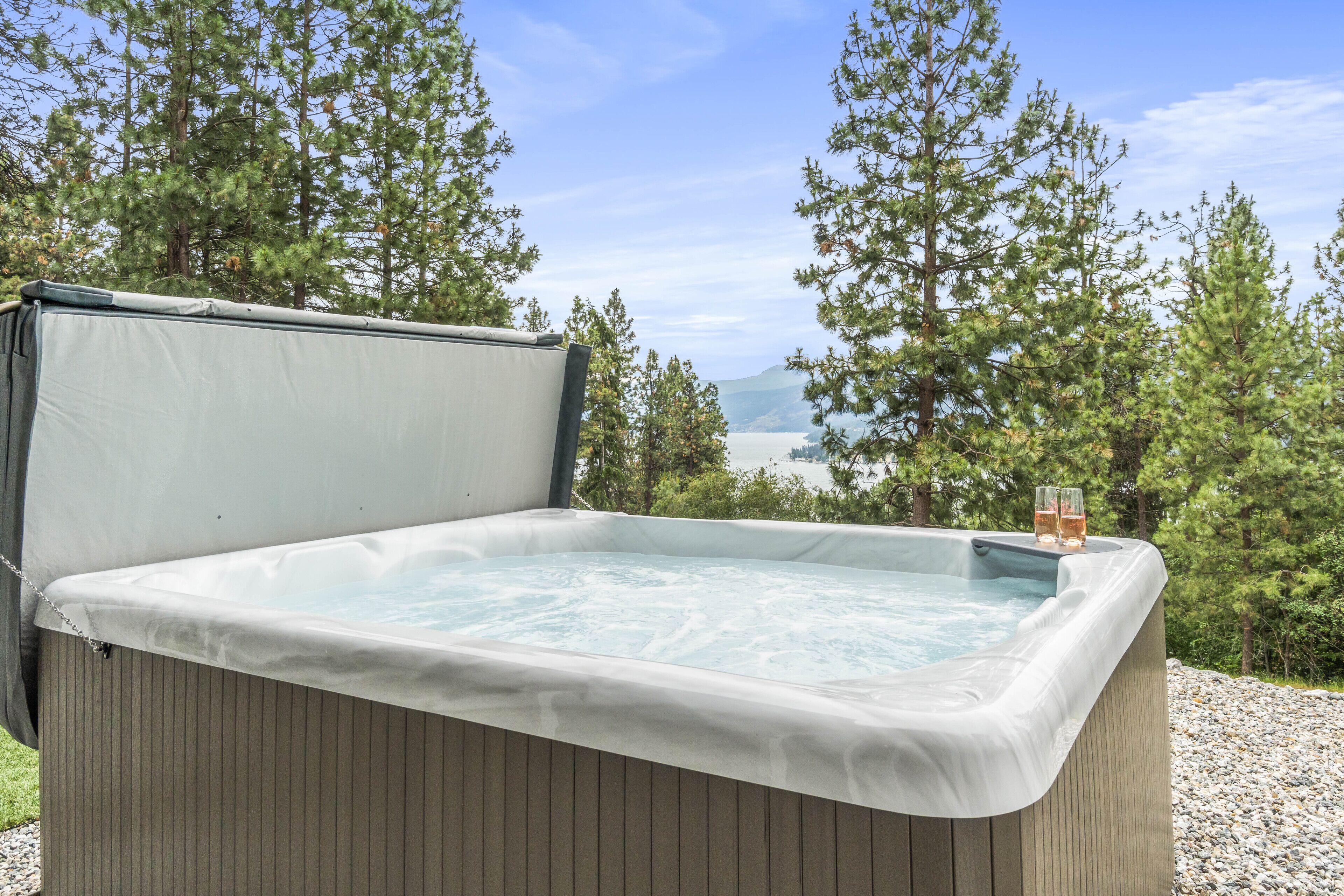 Un bain à remous avec vue sur un lac et des montagnes, entouré d’arbres.