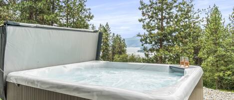 Un bain à remous avec vue sur un lac et des montagnes, entouré d’arbres.