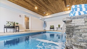 A swimming pool with a stone waterfall feature, a chair with a cushion, and a small table with a plant. - Okanagan Lakeview Oasis, 2 Bed, 2 Bath, Sleeps 6 (Vernon)