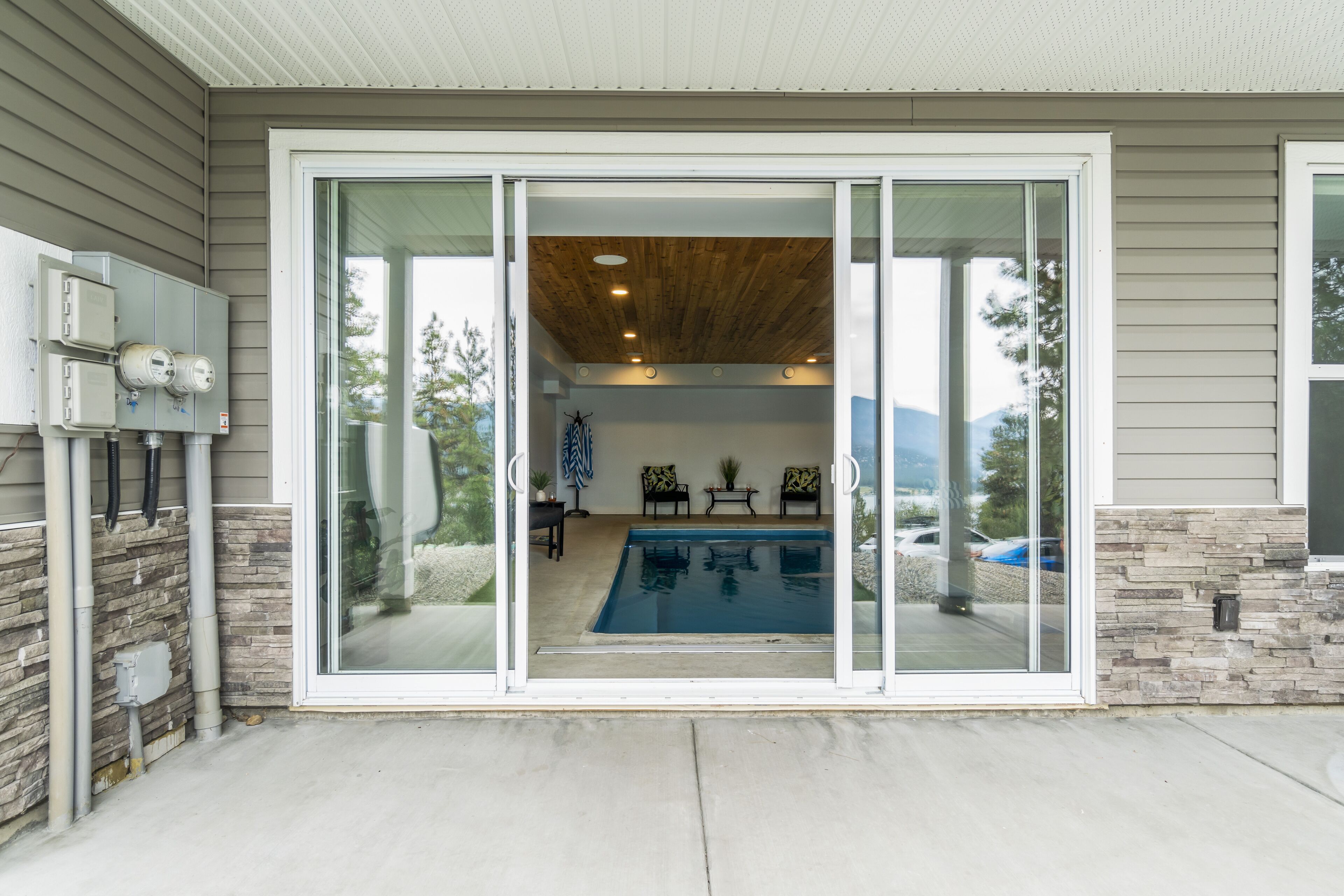 Une maison moderne dotée d’une porte en verre donnant sur un espace piscine, de murs en pierre et d’un plafond en bois.
