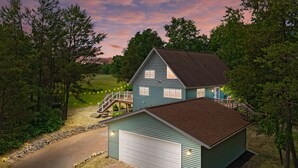Et tosyltet hus med garage, omgivet af træer og en grusvej.