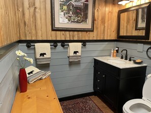 Een badkamer met houten lambrisering, een wastafel met zwarte kastjes en twee handdoeken met berenopdruk.