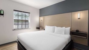 A modern bedroom with a large bed, a window, and built-in lighting. - Ramada by Wyndham Studio Suites Dothan (Dothan)