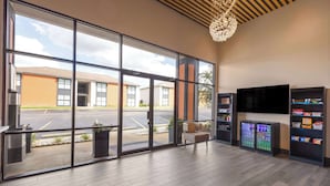 A spacious lobby with large windows, a modern chandelier, a seating area, and vending machines. - Ramada by Wyndham Studio Suites Dothan (Dothan)