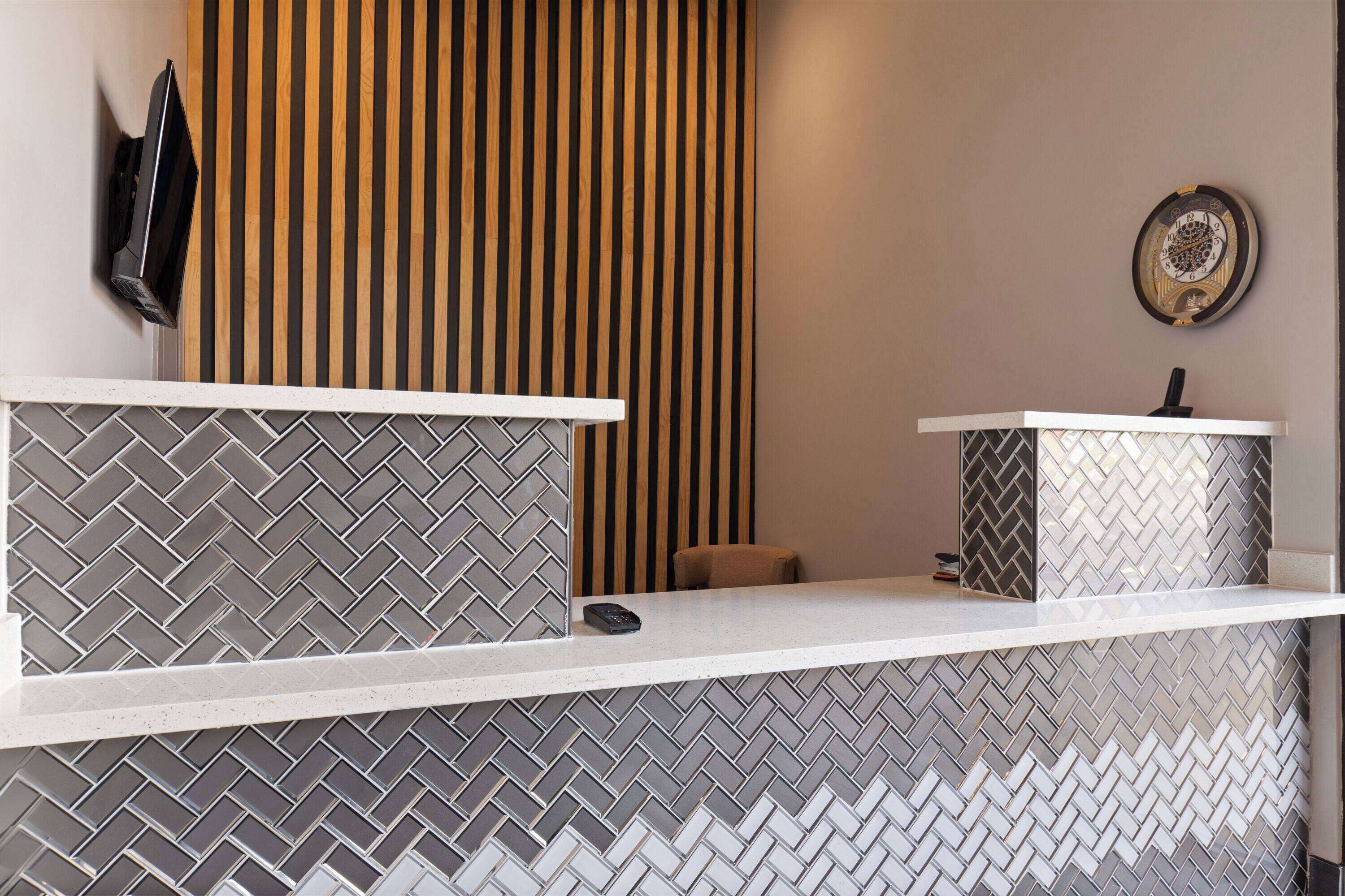 Una zona de recepción con suelo de baldosas en patrón de espiga, pared de listones de madera y un pequeño rincón con asientos.