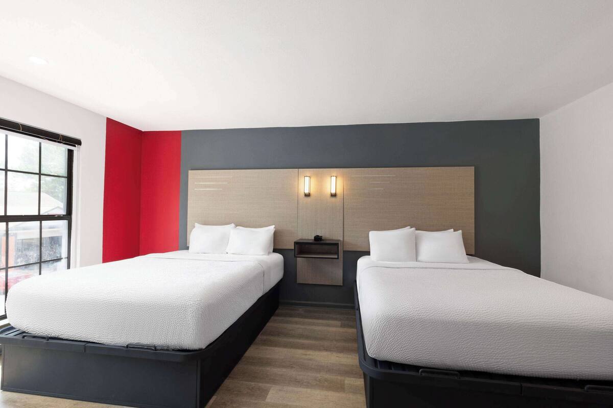 A hotel room with two beds, a nightstand, and a window.
