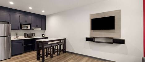 A modern kitchen with dark cabinets, a microwave, a refrigerator, and a dining area with a wooden table and stools.