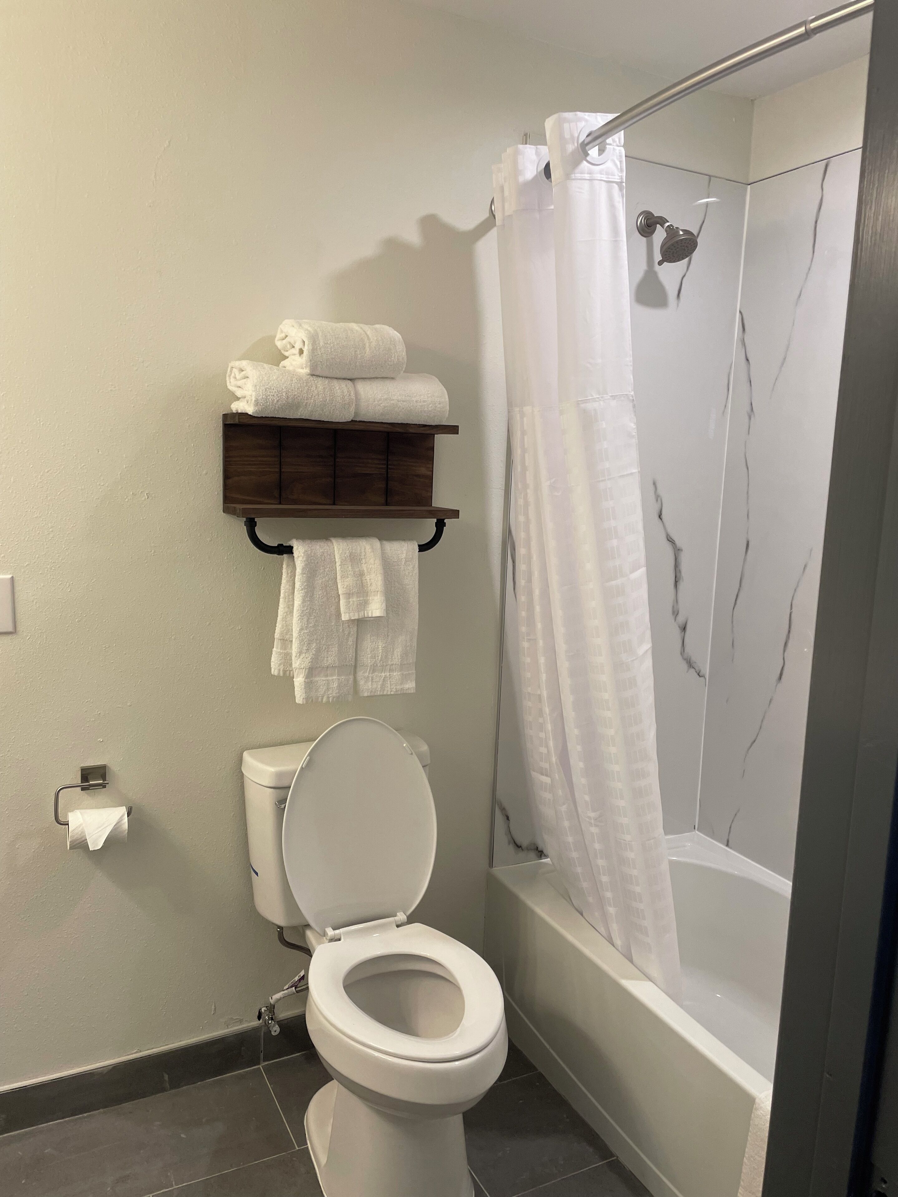 A bathroom with a toilet, a shower with a glass door, and a towel rack with folded towels.