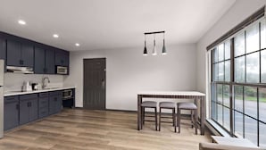 A modern kitchen with dark cabinets, a white countertop, and a wooden dining table with two chairs. - Ramada by Wyndham Studio Suites Dothan (Dothan)