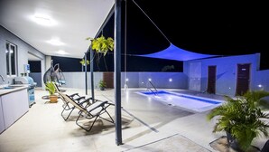 Un espace extérieur avec une piscine, un coin salon couvert, un barbecue et des plantes en pot.