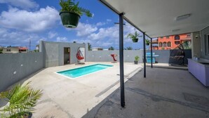 Un espace piscine aménagé sur le toit, avec une piscine rectangulaire, des plantes suspendues et un fauteuil rouge.