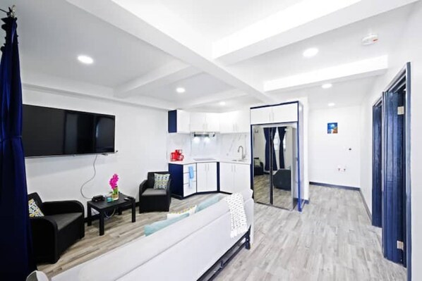 A modern living room with a sofa, coffee table, and TV. A kitchen area is visible in the background. - The Rise at Kendal- Modern Apartment with Pool (Oistins)