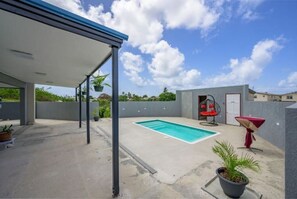 A covered outdoor area with a swimming pool, potted plants, and a red chair. - The Rise at Kendal- Modern Apartment with Pool (Oistins)