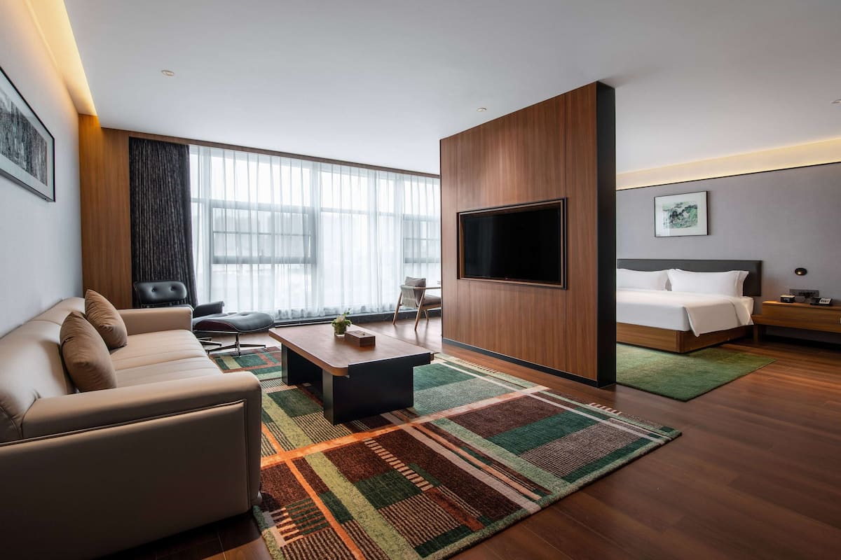 A modern hotel room with a sofa, a coffee table, a TV, a bed, and a green rug.