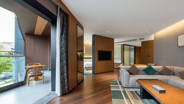 A modern living room with a sofa, coffee table, and a TV. There is a dining area with a table and chairs. The room has wooden flooring and large windows. - Tryp BY Wyndham Zizhou (Neijiang)