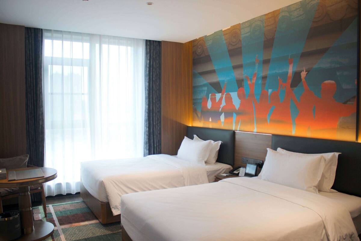 A hotel room with two beds, a desk, and a large abstract painting on the wall.