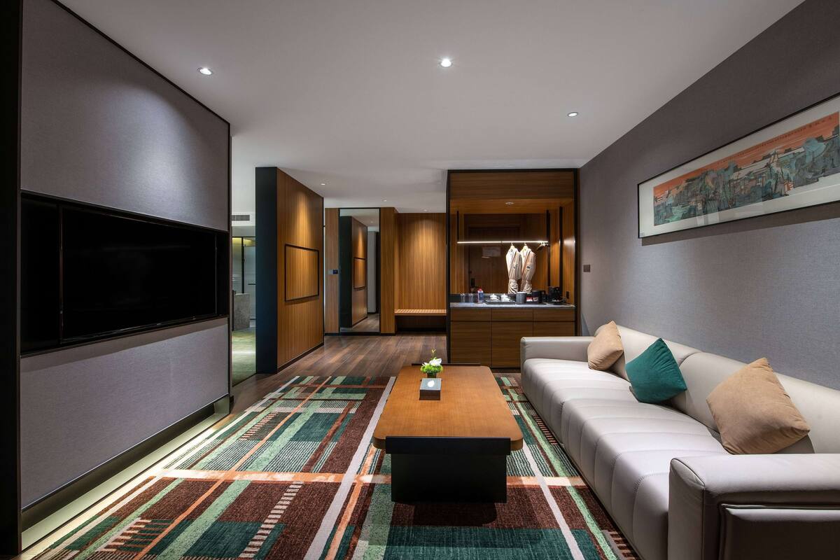 A modern living room with a flat-screen TV, a sofa, a coffee table, and a patterned rug.