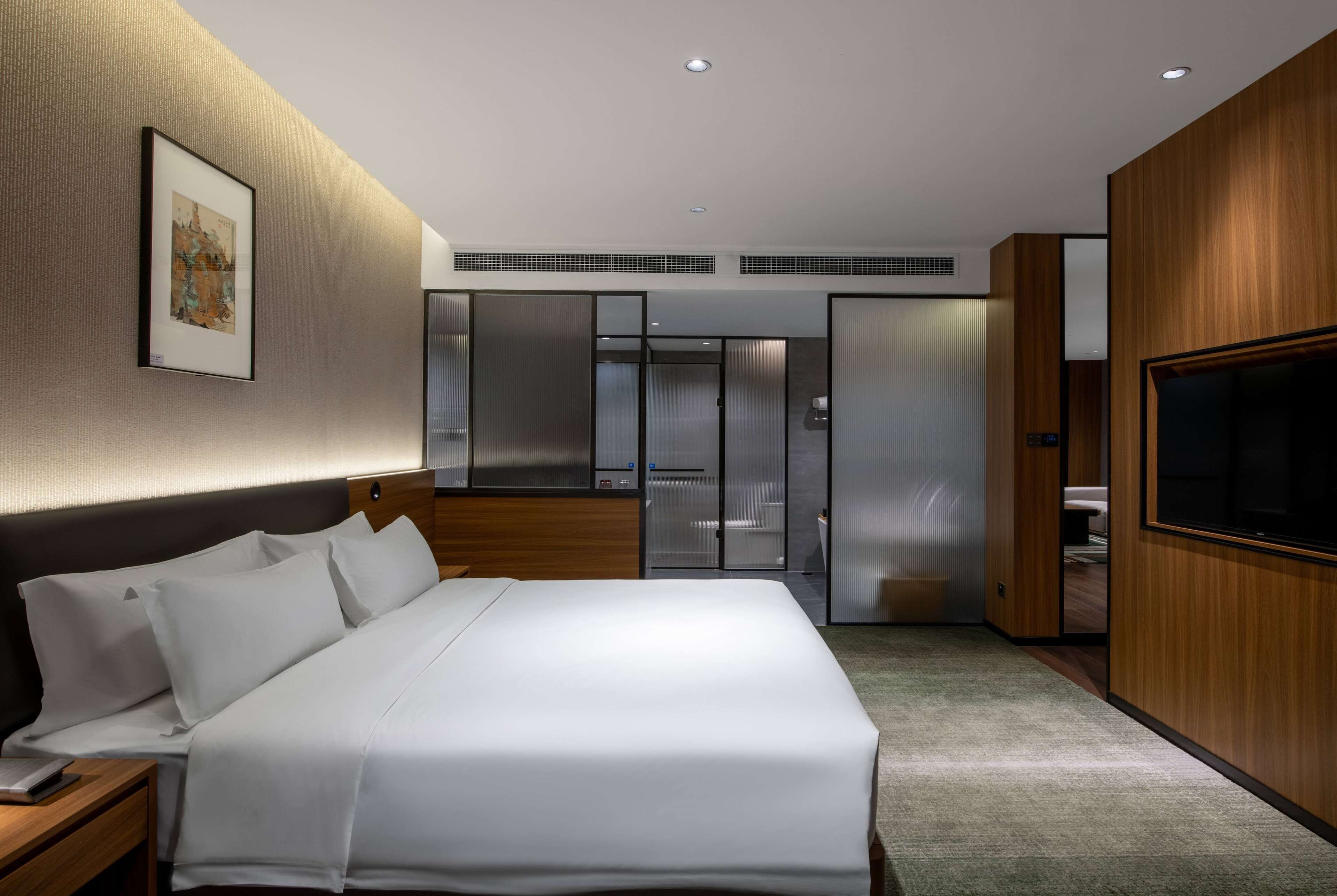 Een moderne hotelkamer met een groot bed, een flatscreen televisie, een houten hoofdbord, een ingelijste foto aan de muur en een inloopkast.