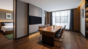 A modern hotel room with a wooden floor, a large bed, a TV mounted on the wall, a dining table with chairs, and large windows with curtains. - Tryp BY Wyndham Zizhou (Neijiang)