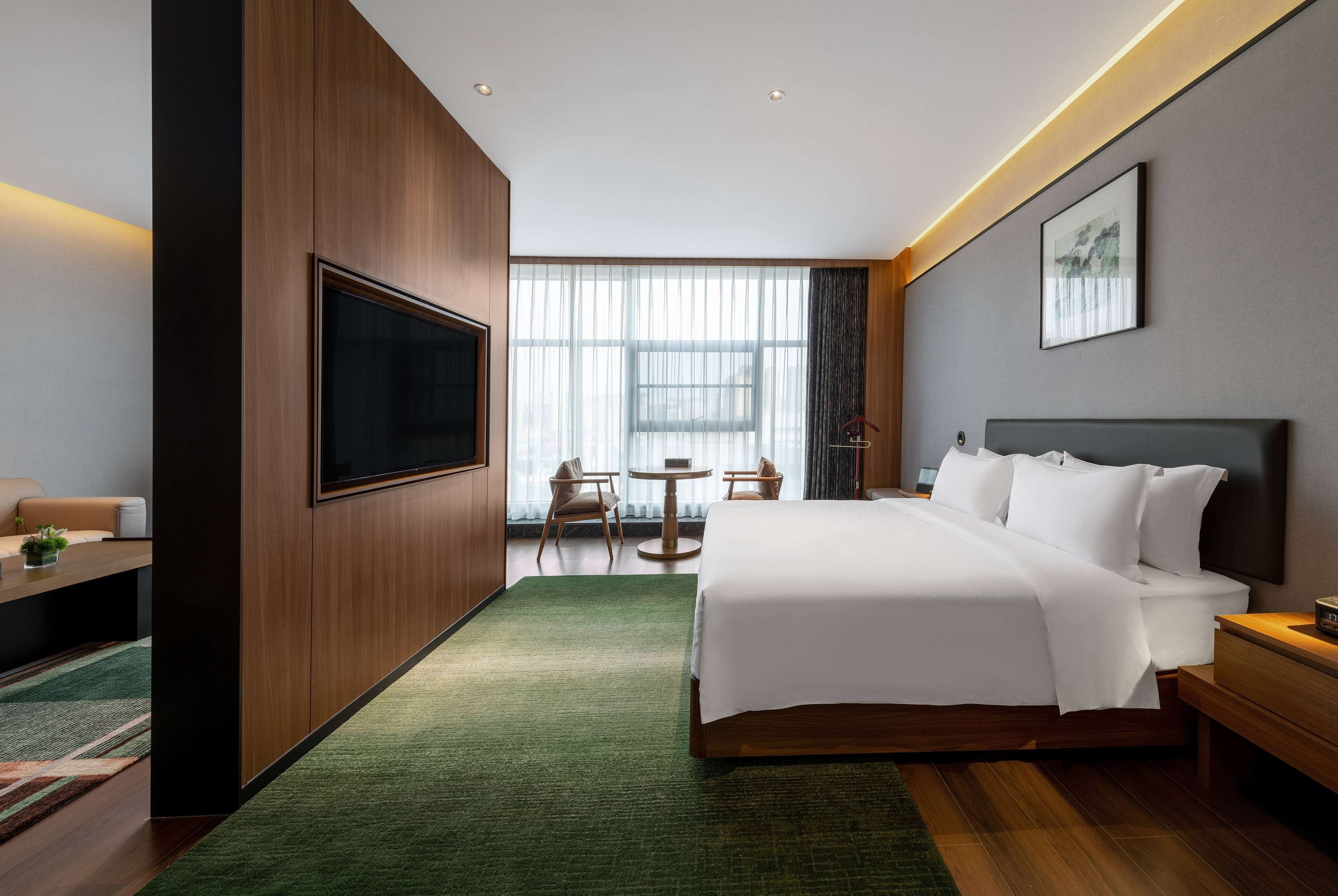 Ein modernes Hotelzimmer mit einem großen Bett, einem Fernseher, einem Esstisch und Blick ins Freie.