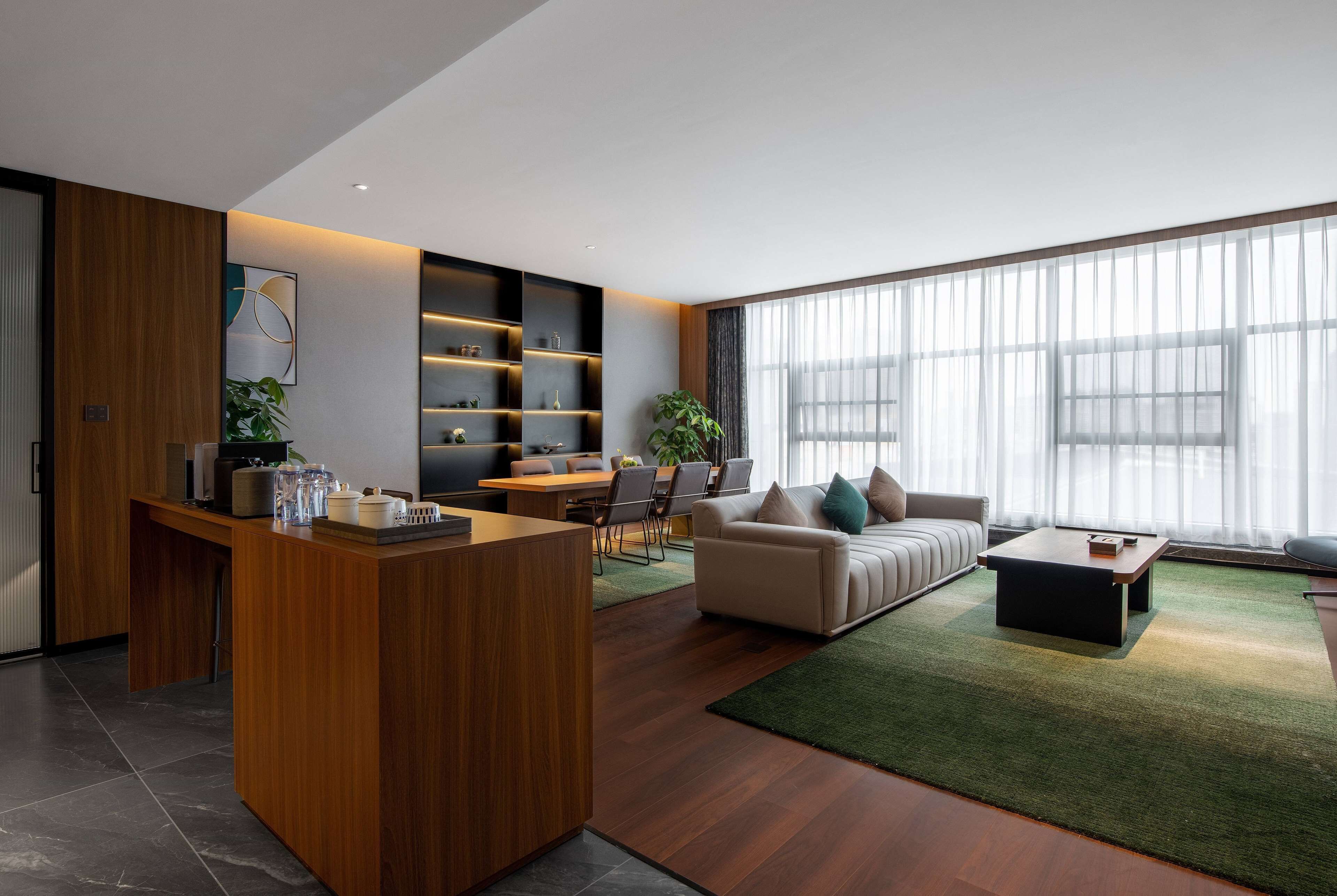 A modern living room with a wooden reception desk, a sofa, a coffee table, and a dining area with chairs and a table.