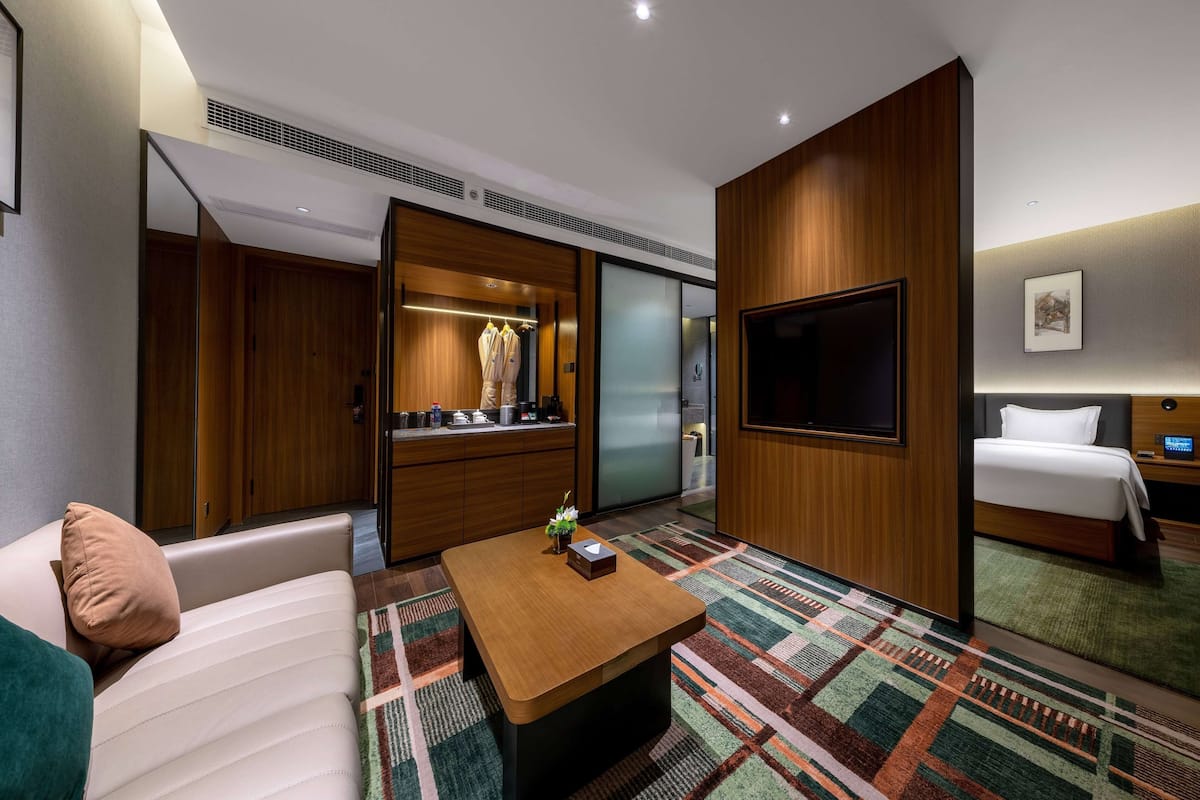 A hotel room with a sofa, a wooden coffee table, a bed, a TV, and a wardrobe.