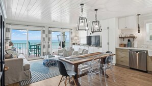 A modern interior with a dining area, kitchen, and a balcony with a view. - AZUL | Beachfront Unit | Panoramic Gulf Views (Santa Rosa Beach)