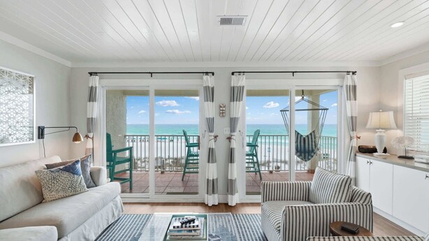 A room with a sofa, armchairs, a coffee table, a view of the ocean through large sliding doors, and a hanging chair on a balcony. - AZUL | Beachfront Unit | Panoramic Gulf Views (Santa Rosa Beach)