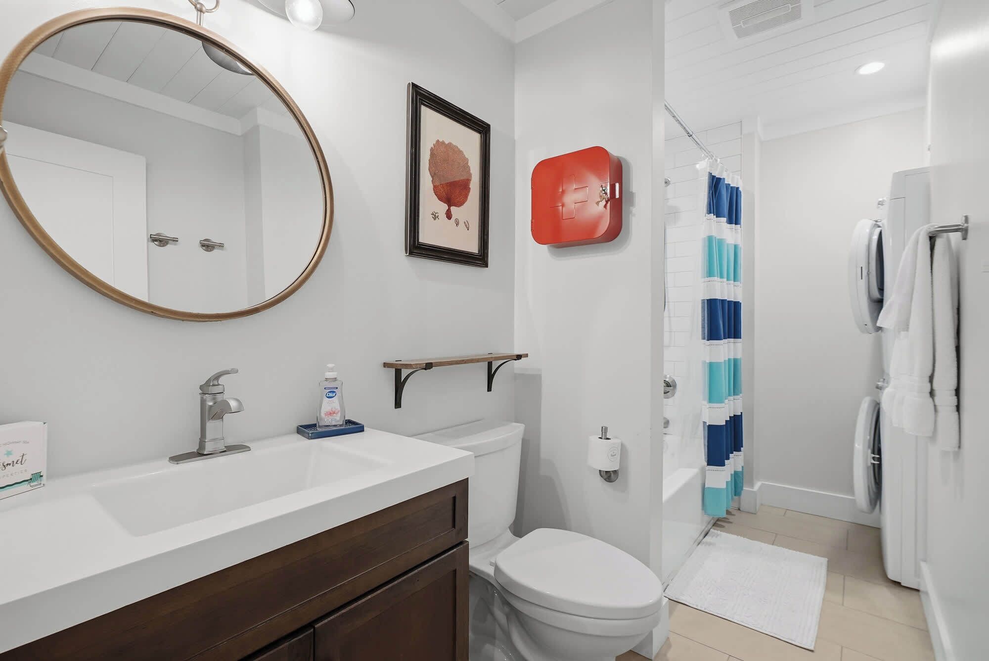 A bathroom with a white sink, a toilet, a shower with blue curtains, and a framed picture on the wall.
