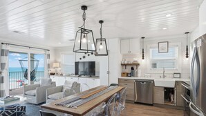 A modern kitchen with a dining area, a TV, and a view of the ocean. - AZUL | Beachfront Unit | Panoramic Gulf Views (Santa Rosa Beach)