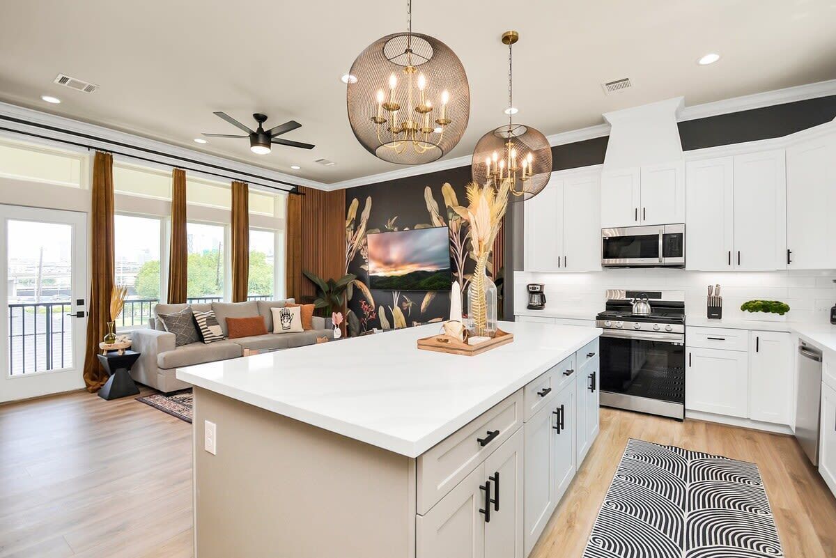Et moderne køkken med hvide skabe, en central ø og et spiseområde med sofa og gardiner.