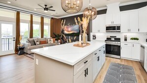 A modern kitchen with white cabinets, a central island, and a dining area with a sofa and curtains. - The Oasis Checkmate HTX Rooftop (Houston)